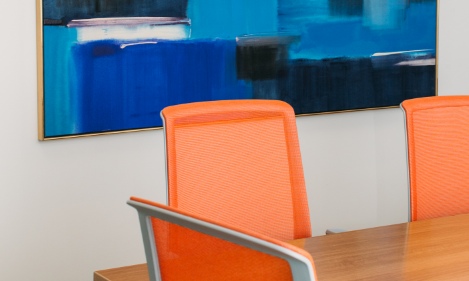 Orange office chairs around a table. A large abstract blue painting is hanging on the wall behind it.